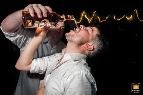 A groomsman offers whiskey to the groom at La Arbolada Rosario, Santa Fe, Argentina. The  wedding photo shows a candid moment of the groom drinking.
